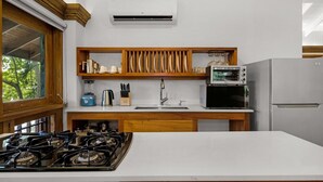 A modern kitchen with a gas stove, microwave, refrigerator, and wooden shelves with kitchen utensils. - Idle Awhile Beach - Family Suite in Negril (Negril)