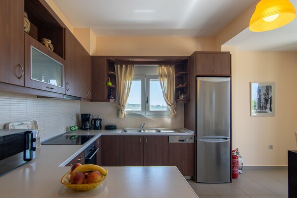 A modern kitchen with wooden cabinets, a stainless steel refrigerator, a dishwasher, and a window with curtains.