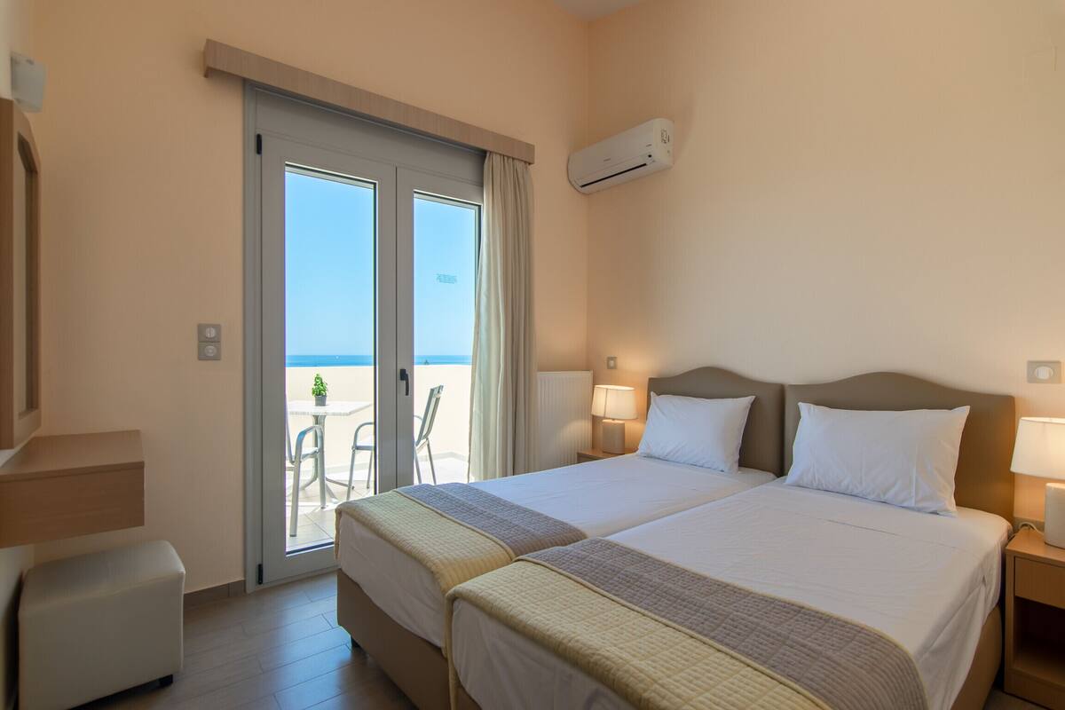 A hotel room with two beds, a balcony with a table and chairs, and an air conditioning unit.
