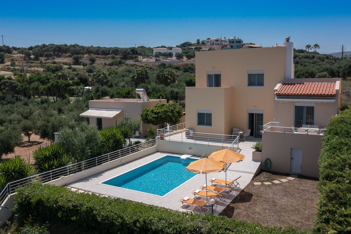 A modern villa with a swimming pool, outdoor seating, and a view of the surrounding landscape.
