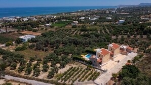 An aerial view of a coastal property with multiple buildings, a swimming pool, and olive groves. - Yanni's villas (Rethymno)