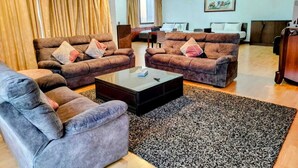 A spacious living room with a large coffee table, two sofas, and a grey armchair. There is a dining area in the background with a chandelier. - 4-bedroom apartment in marvelous City with AC, fitness room (City)