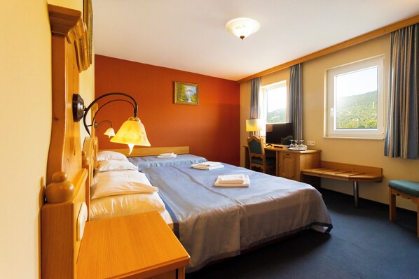 A hotel room with two beds, a desk, a chair, a TV, and a window with curtains. - Aquamarina Hotel Visegrád (Visegrád)