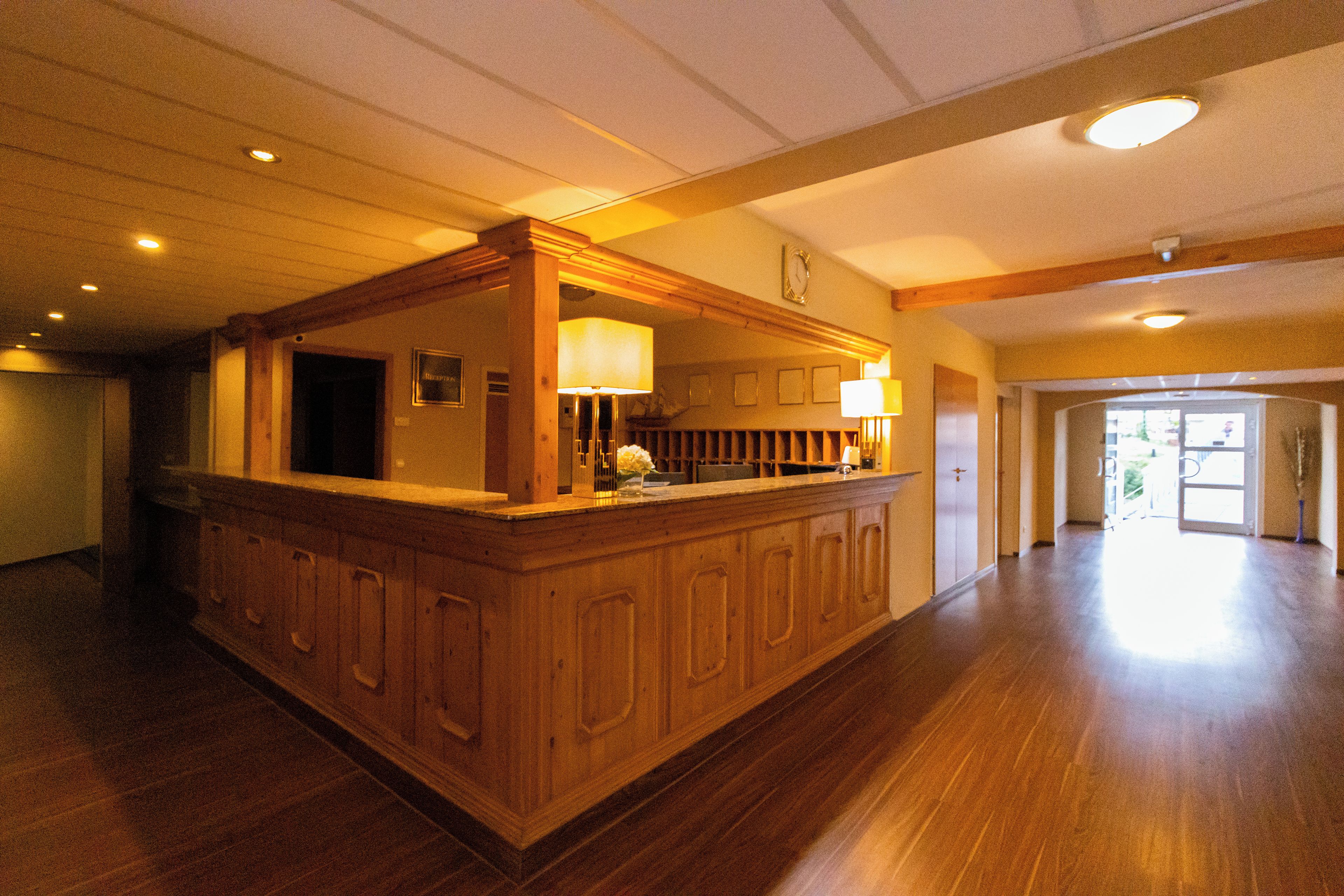 A spacious lobby with a wooden reception desk, a clock on the wall, and a large open area leading to an exit.