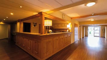 A spacious lobby with a wooden reception desk, a clock on the wall, and a large open area leading to an exit.