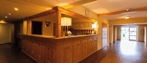 A spacious lobby with a wooden reception desk, a clock on the wall, and a large open area leading to an exit.