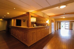 A spacious lobby with a wooden reception desk, a clock on the wall, and a large open area leading to an exit. - Aquamarina Hotel Visegrád (Visegrád)