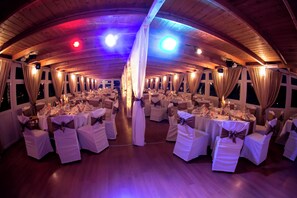 A banquet hall with round tables and white chairs, featuring a wooden ceiling and large windows. - Aquamarina Hotel Visegrád (Visegrád)