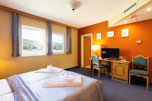 Habitación de hotel con cama, escritorio con televisor y vistas al exterior a través de una ventana.