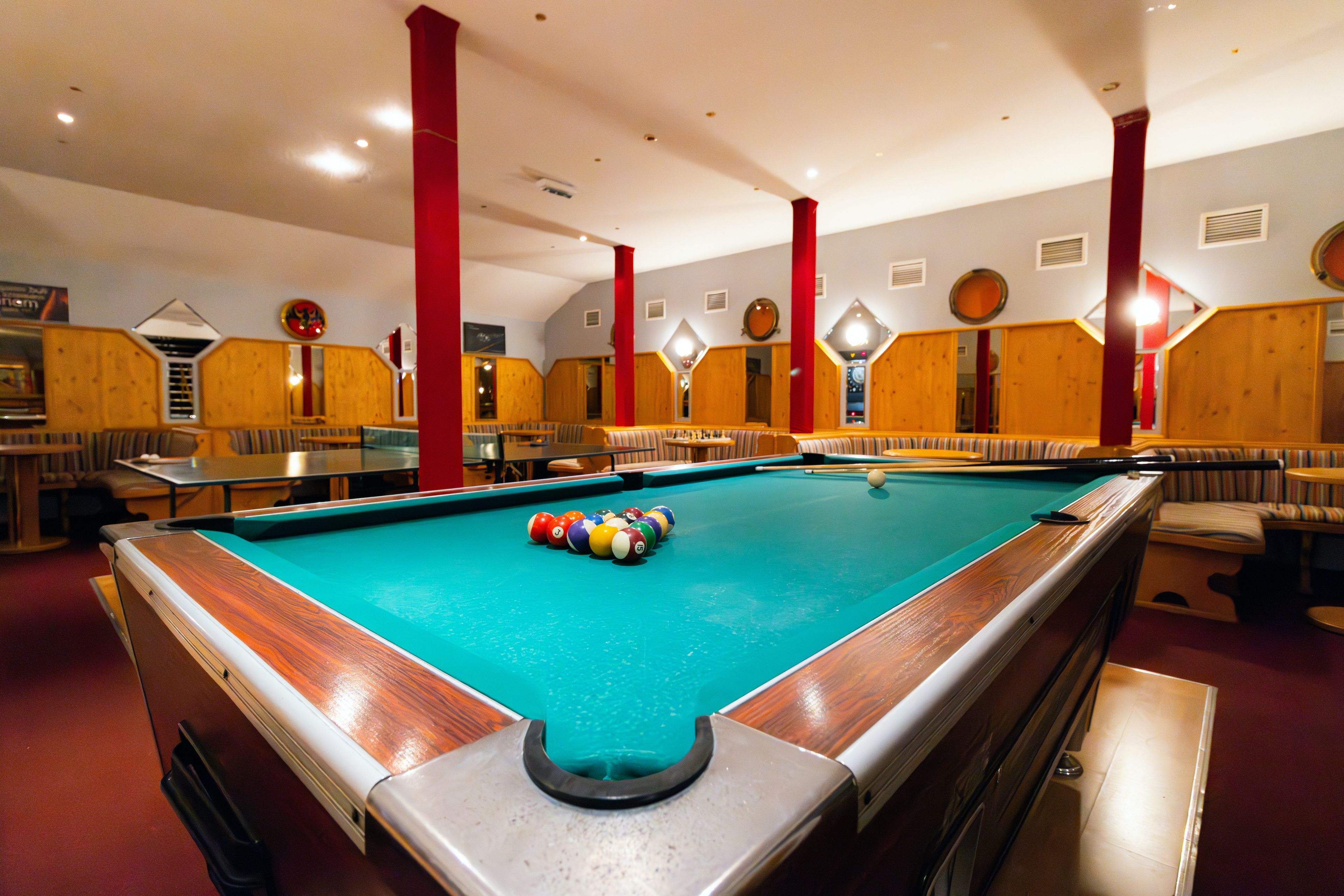 A pool table with balls, wooden benches, and a red pillar.