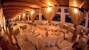 Une salle de banquet avec des tables rondes dressées pour le repas, des nappes blanches et des chaises recouvertes de housses blanches.