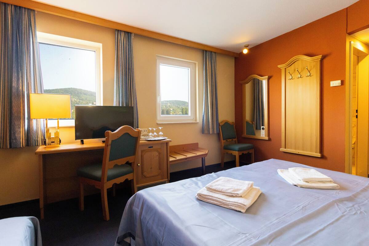 Ein Hotelzimmer mit einem Bett, einem Schreibtisch mit Stuhl, einem Fernseher und einem Fenster mit Vorhängen.