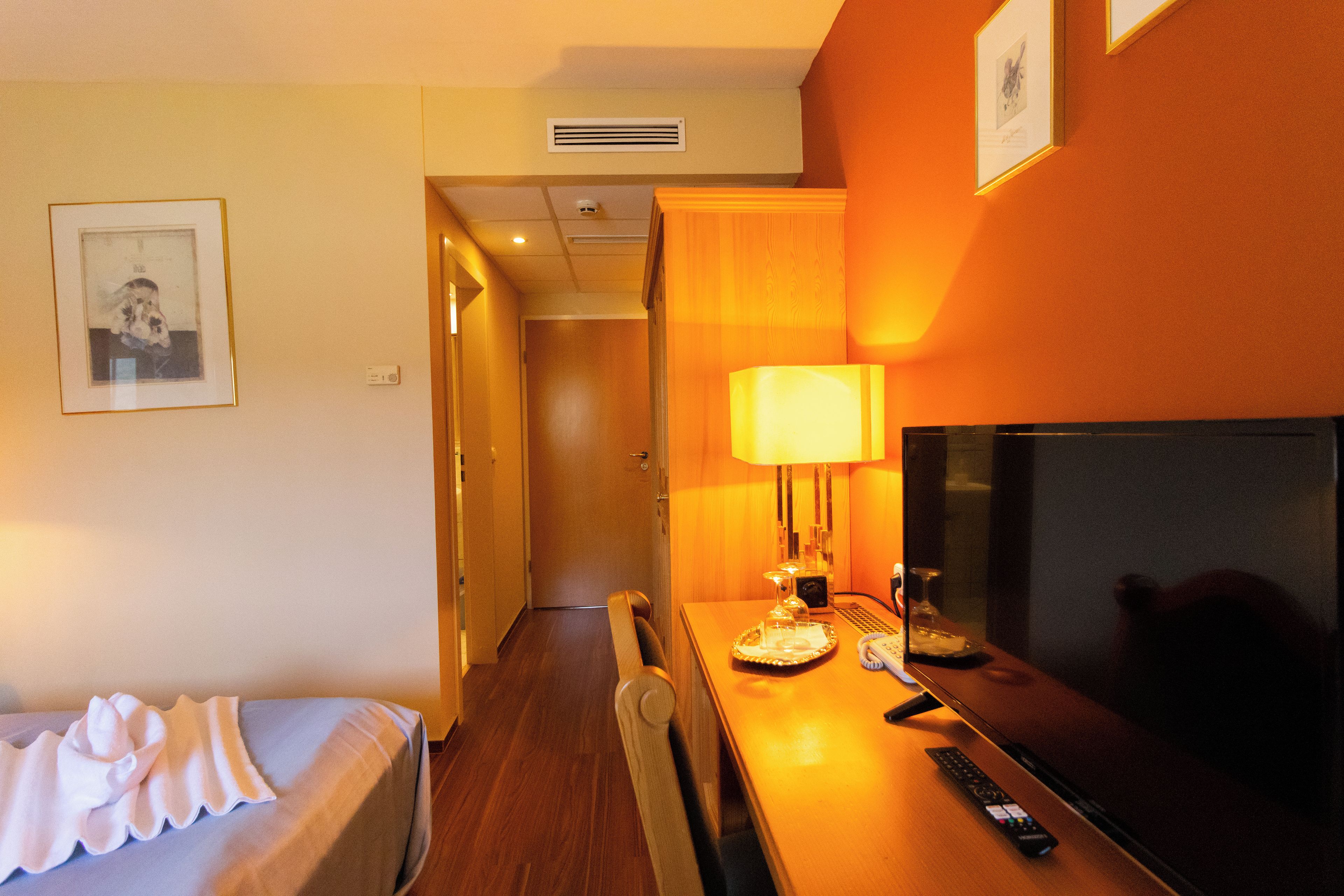 A hotel room with a bed, a dining table with a lamp, a remote control, and a television.