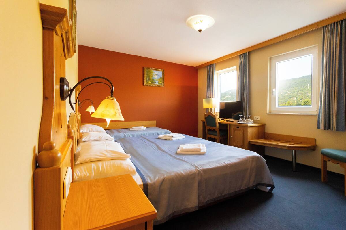 Ein Hotelzimmer mit zwei Betten, einem Schreibtisch, einem Stuhl, einem Fernseher und einem Fenster mit Vorhängen.