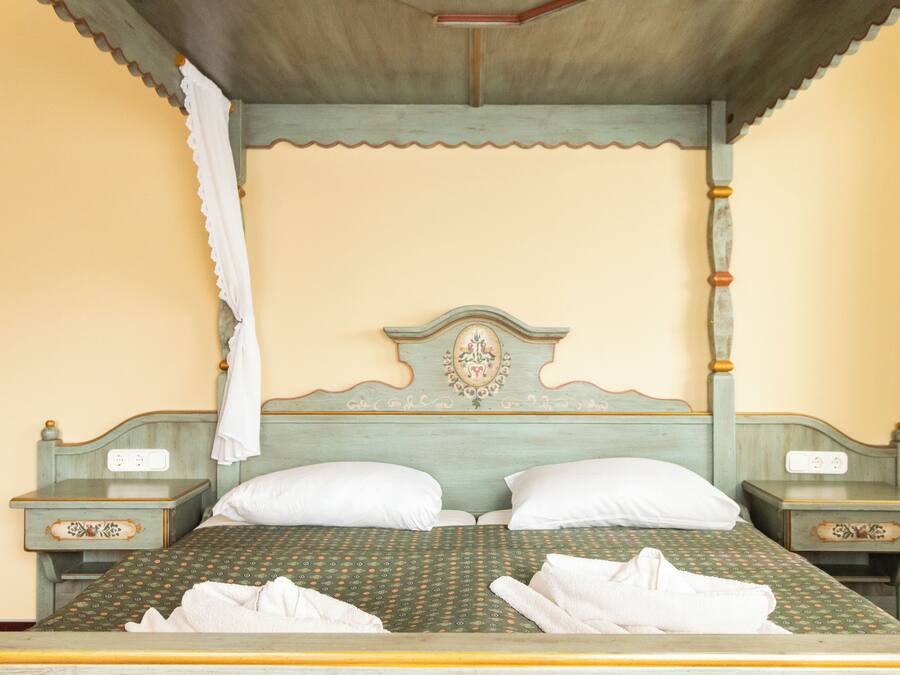 Una cama con colcha estampada, dos almohadas y un cabecero con un escudo decorativo. Hay dos mesitas de noche con cajones y un enchufe en cada una.