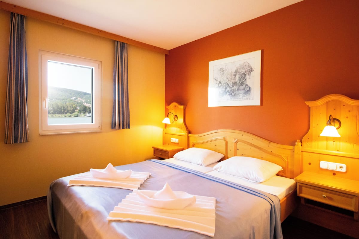 Ein Hotelzimmer mit einem großen Bett, zwei Nachttischen, einem Fenster mit Vorhängen und einem Bild an der Wand.