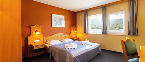 A hotel room with a bed, two bedside tables with lamps, a chair, and a window with curtains.