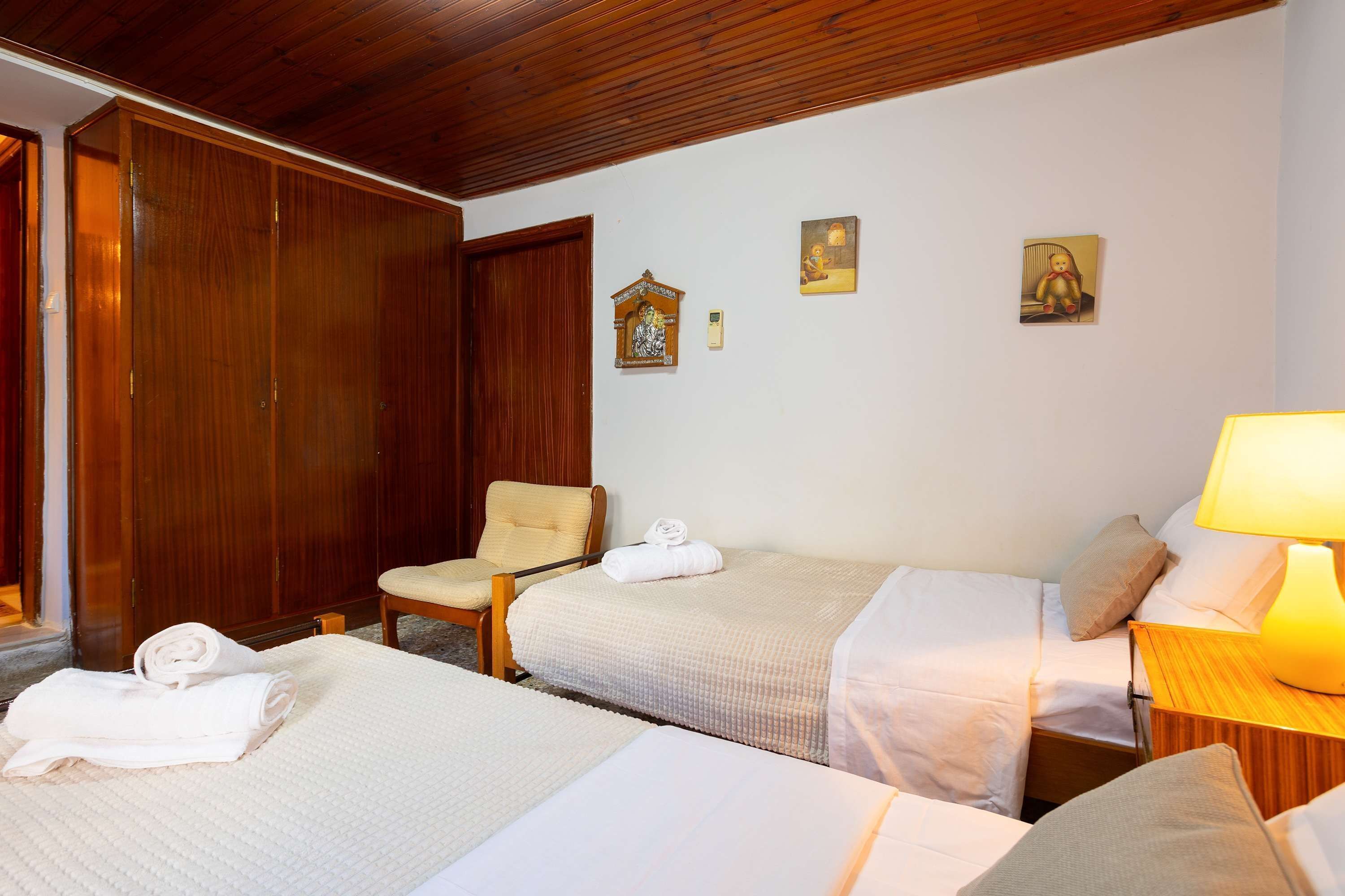 Ein Hotelzimmer mit zwei Betten, einem Holzschrank, einem Sessel und einem kleinen Tisch mit einer Lampe.
