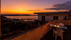 Una terrazza con un tavolo apparecchiato per due persone, vista su un corpo d'acqua e una costa lontana.