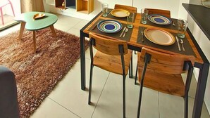 Un comedor con una mesa de madera dispuesta para cuatro personas, rodeada de sillas. Un televisor está montado en la pared, y un accesorio de iluminación decorativo cuelga sobre la mesa.
