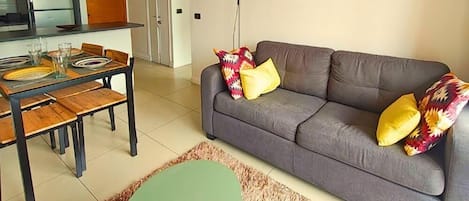 A modern living room with a grey sofa, colorful cushions, a green coffee table, and a large abstract painting on the wall.