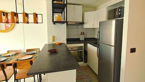 Una cocina compacta con una isla central, un comedor con sillas de madera y un horno empotrado.