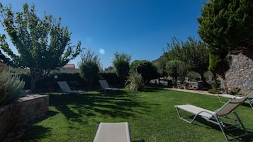 Un giardino sul retro con prato, due poltrone relax, un muro in pietra e diversi alberi.