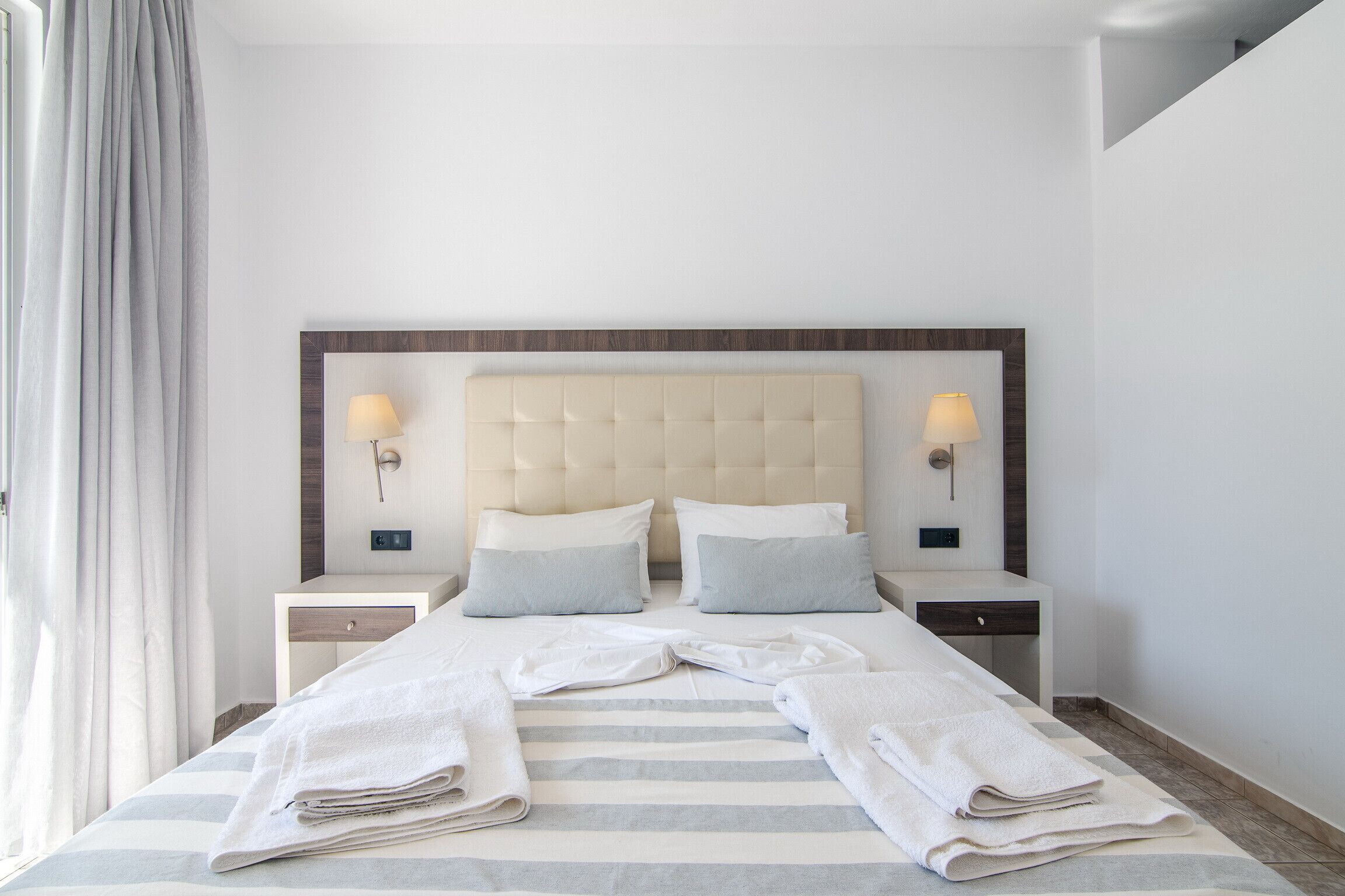 A hotel room with a large bed, two bedside tables, a headboard, and two wall-mounted lamps.