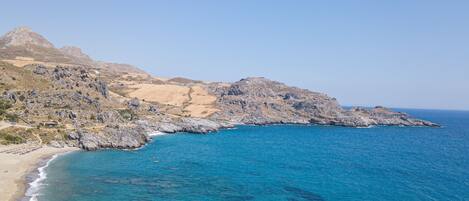 A coastal landscape with rocky terrain and a clear blue sea.