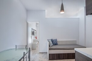 Une pièce moderne et minimaliste, dotée d’une table à manger en verre, d’une banquette intégrée avec des coussins et d’un luminaire suspendu.