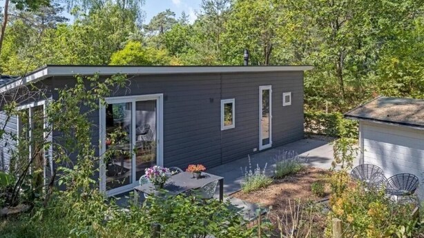 A modern, compact house with a small patio, surrounded by lush greenery.