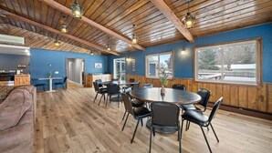 Une pièce spacieuse avec un plafond en bois, un coin repas comprenant une table ronde et des chaises, et de grandes fenêtres offrant une vue sur l’extérieur.