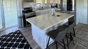 Een moderne keuken met witte kasten, een groot kookeiland met barkrukken, een roestvrijstalen koelkast en een gasfornuis.