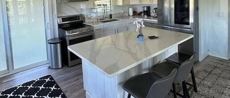 A modern kitchen with white cabinets, a large island with bar stools, a stainless steel refrigerator, and a gas stove.