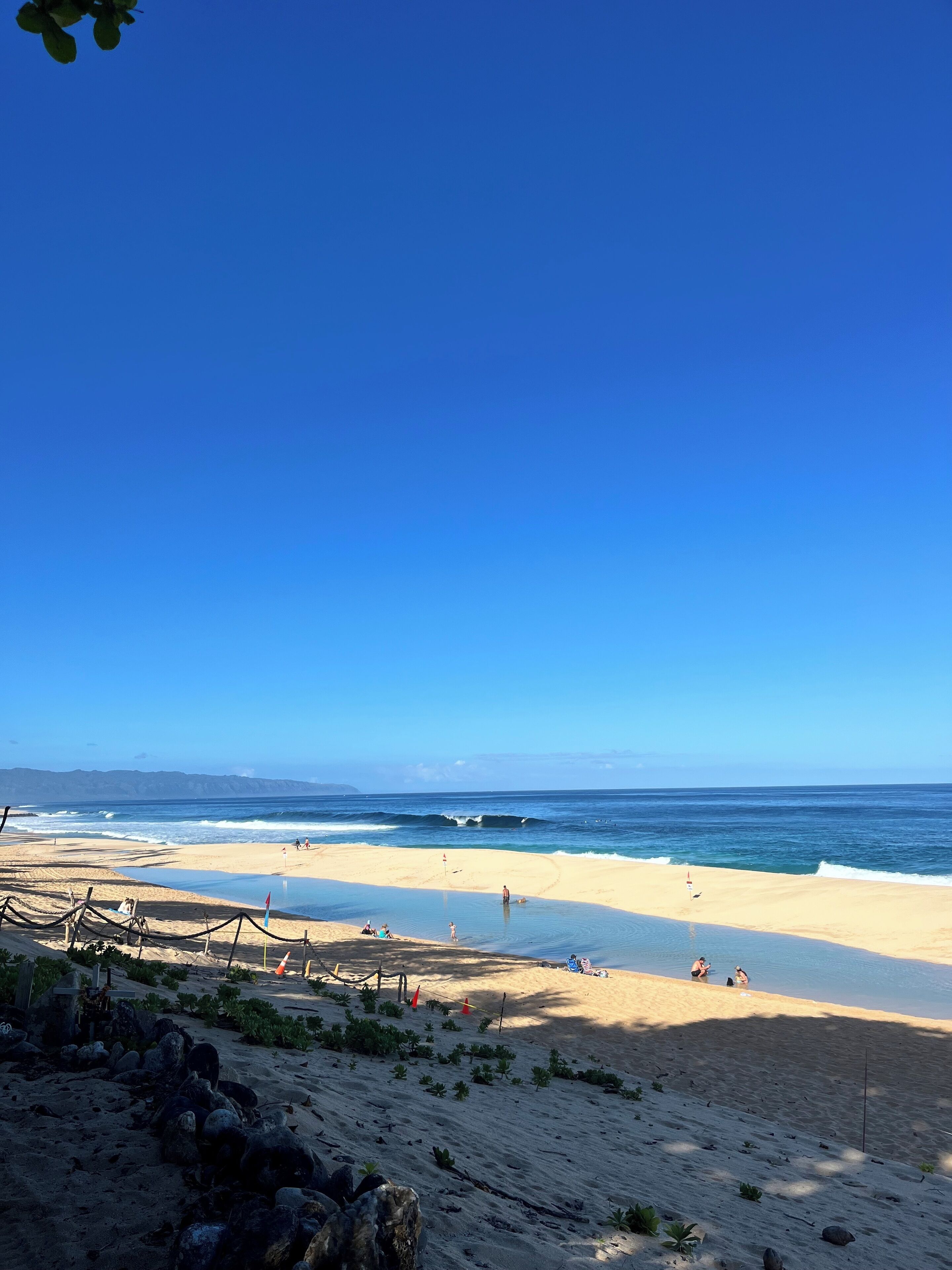 A beach with clear skies, calm waves, and a few people.