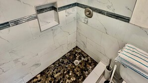 Een badkamer met witte marmeren tegels, een douche met handdouche, een toilet en een raam met uitzicht.