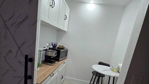 Una cocina compacta con gabinetes blancos, una pequeña encimera y una zona de comedor con dos taburetes.