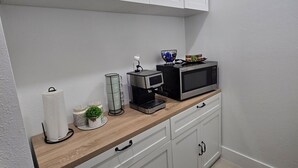 Una cocina moderna con armarios blancos, encimera de madera, cafetera, microondas y una pequeña planta en maceta.