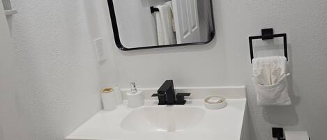 A bathroom with a white sink, black faucet, and a mirror above it. There is a towel rack with a white towel and a black towel holder.