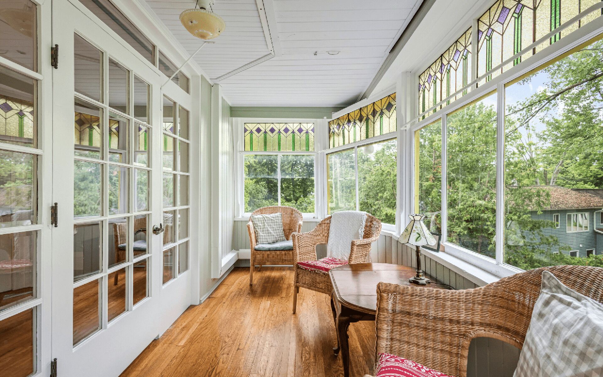 A sunroom with large windows, wicker furniture, and a wooden floor.