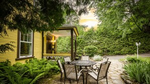 A yellow house with a porch, a stone patio with a table and chairs, and lush greenery. - Victorian inn dating from 1864 with spa - sleeps 18 (WATERLOO)