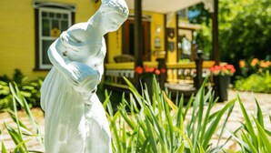 A statue in a garden with a yellow building in the background. - Victorian inn dating from 1864 with spa - sleeps 18 (WATERLOO)