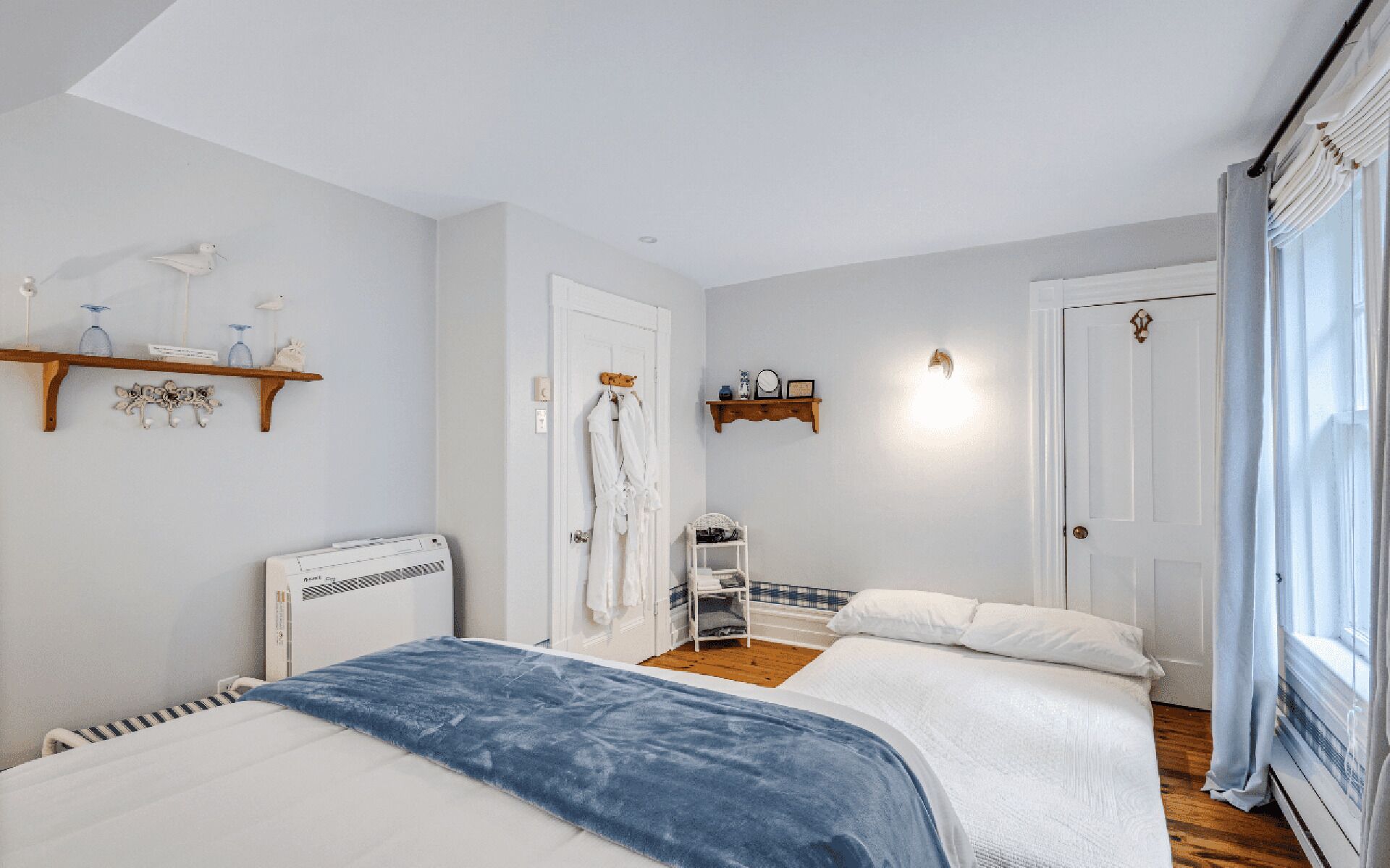 A bedroom with two beds, a radiator, a shelf with decorative items, and a door with a towel rack.