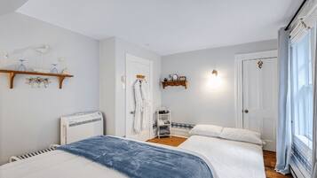 A bedroom with two beds, a radiator, a shelf with decorative items, and a door with a towel rack.