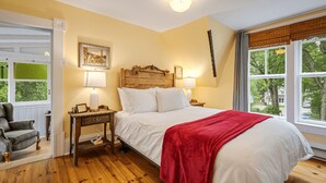 A bedroom with a wooden bed, two bedside lamps, a nightstand, a chair, and a window with blinds. - Victorian inn dating from 1864 with spa - sleeps 18 (WATERLOO)
