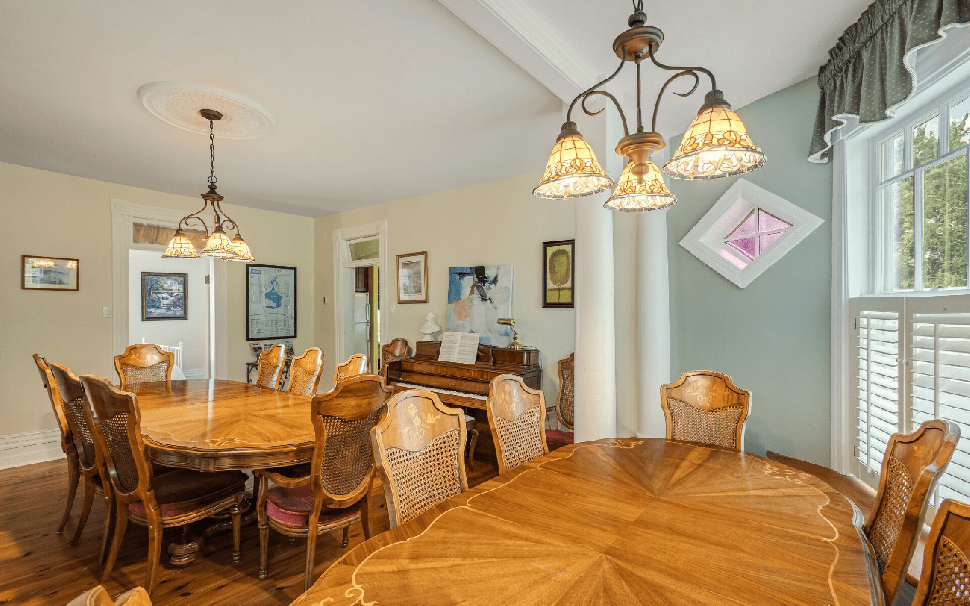 Une salle à manger avec une grande table et des chaises en bois, un piano et un lustre.