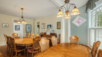 Une salle à manger avec une grande table et des chaises en bois, un piano et un lustre.