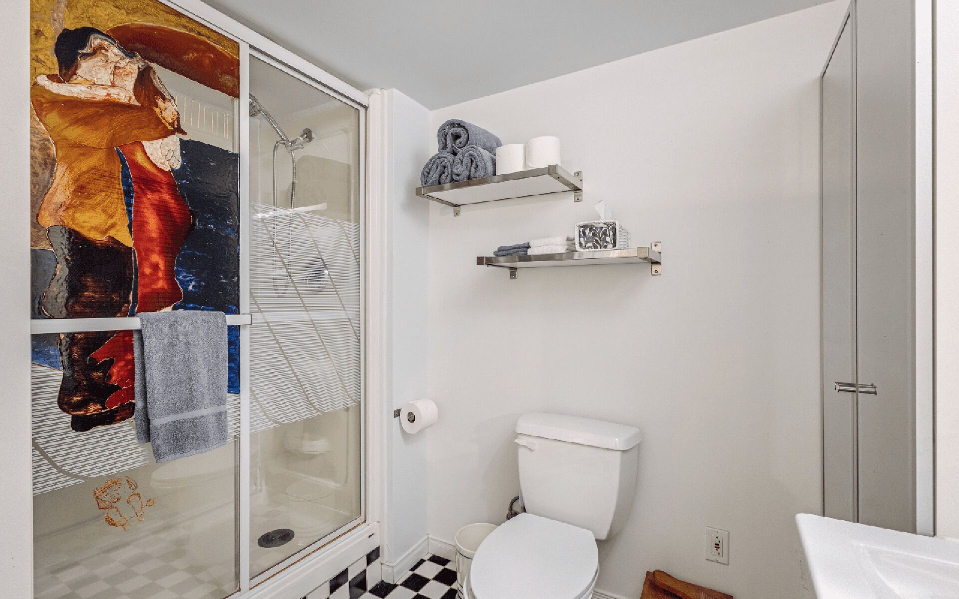 A bathroom with a glass shower enclosure, a toilet, and two shelves with towels and toiletries.