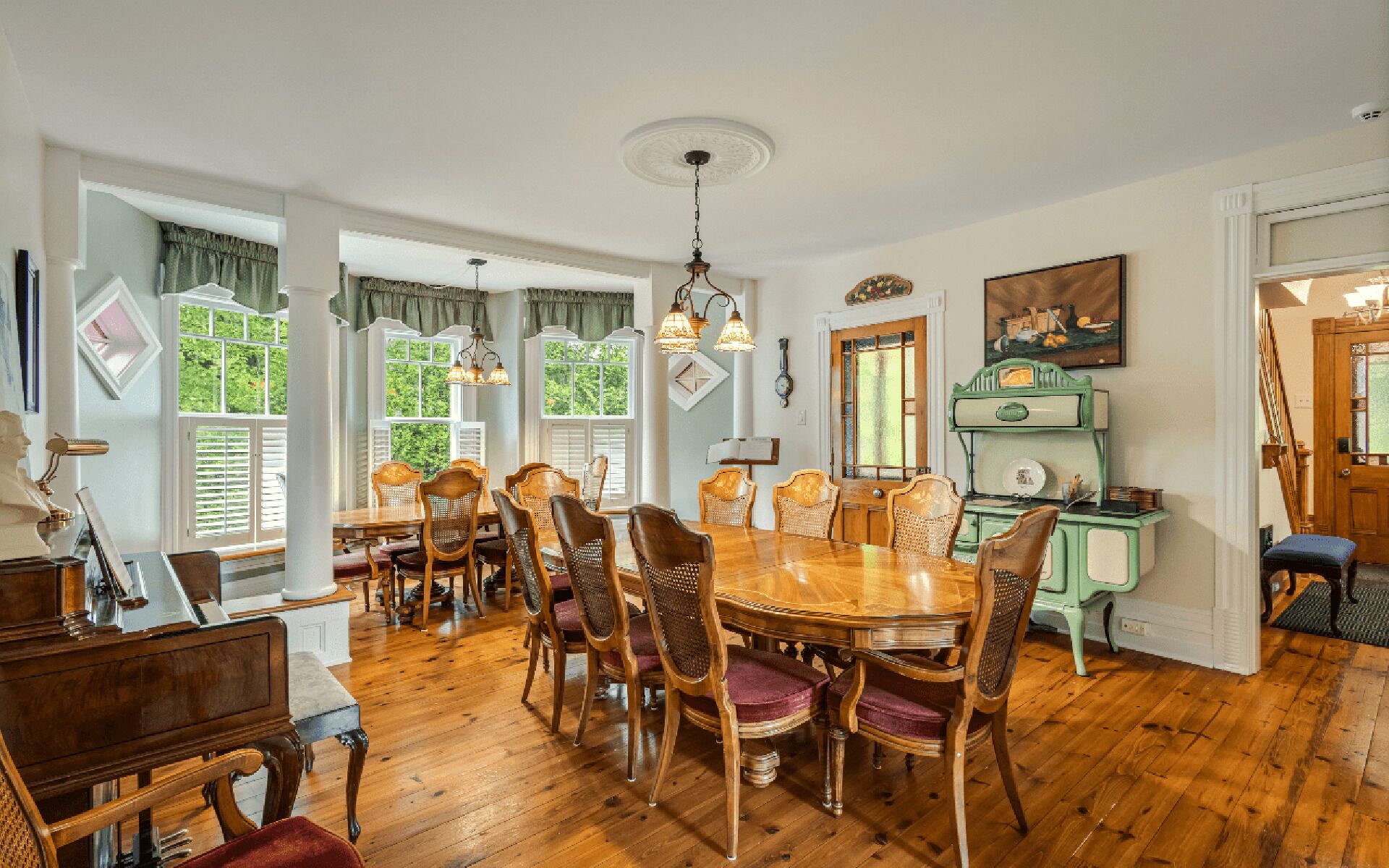 Comedor con mesa y sillas de madera, ventanas grandes con contraventanas y un refrigerador de estilo vintage.