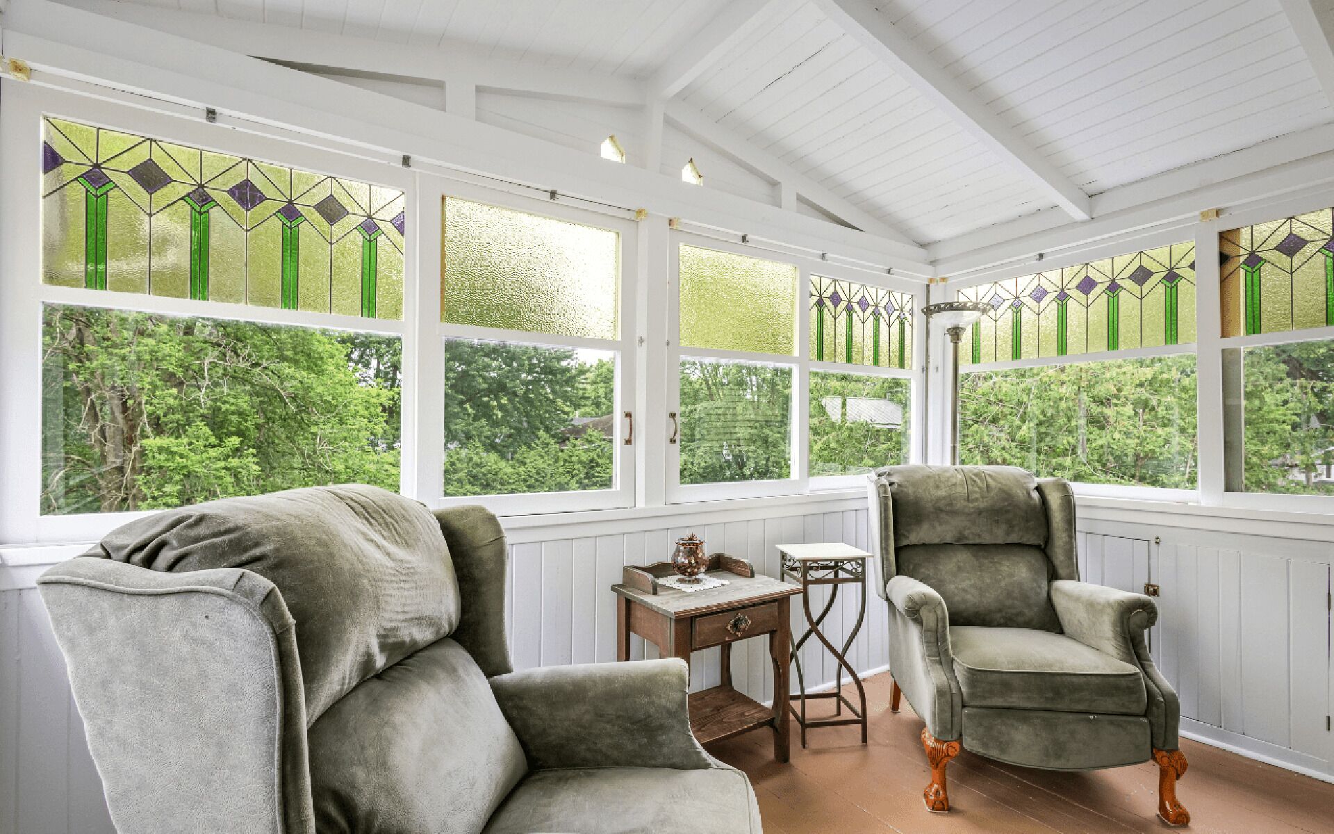A conservatory with two armchairs, a small table, and a view of greenery.